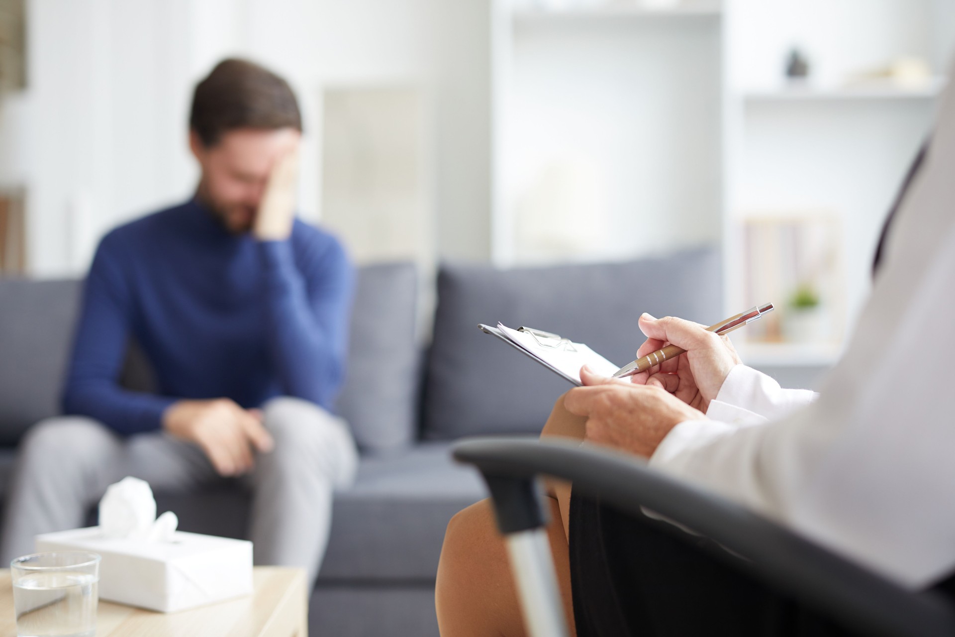 Close-up of unrecognizable psychiatrist sitting on chair and making notes while analyzing mental state of patient during therapy session